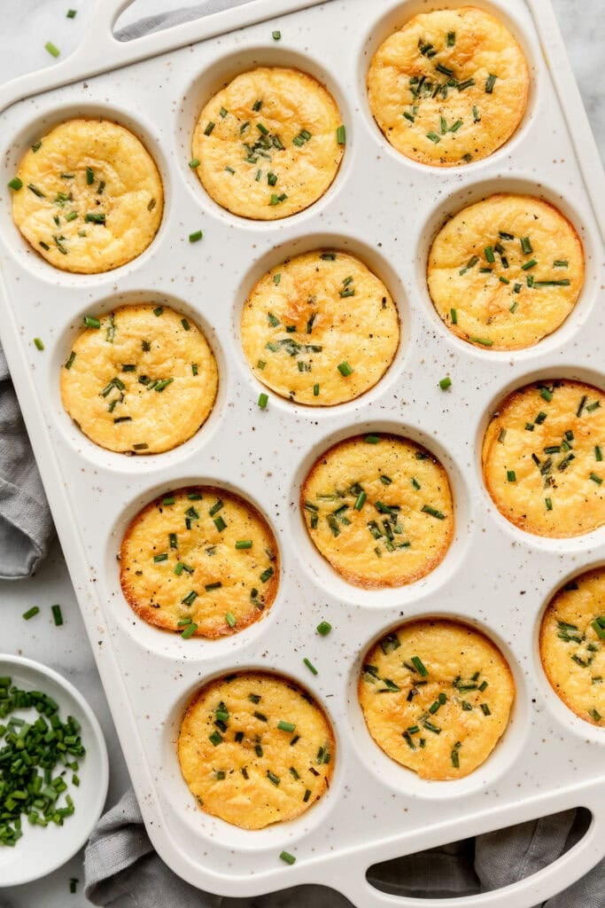 Overhead view of freshly baked egg bites in a muffin pan topped with fresh chives and flakey sea salt. 