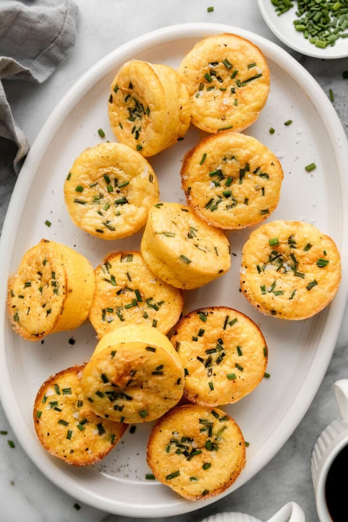 Close up view of a plate of egg bites topped with fresh chives and flakey sea salt. 