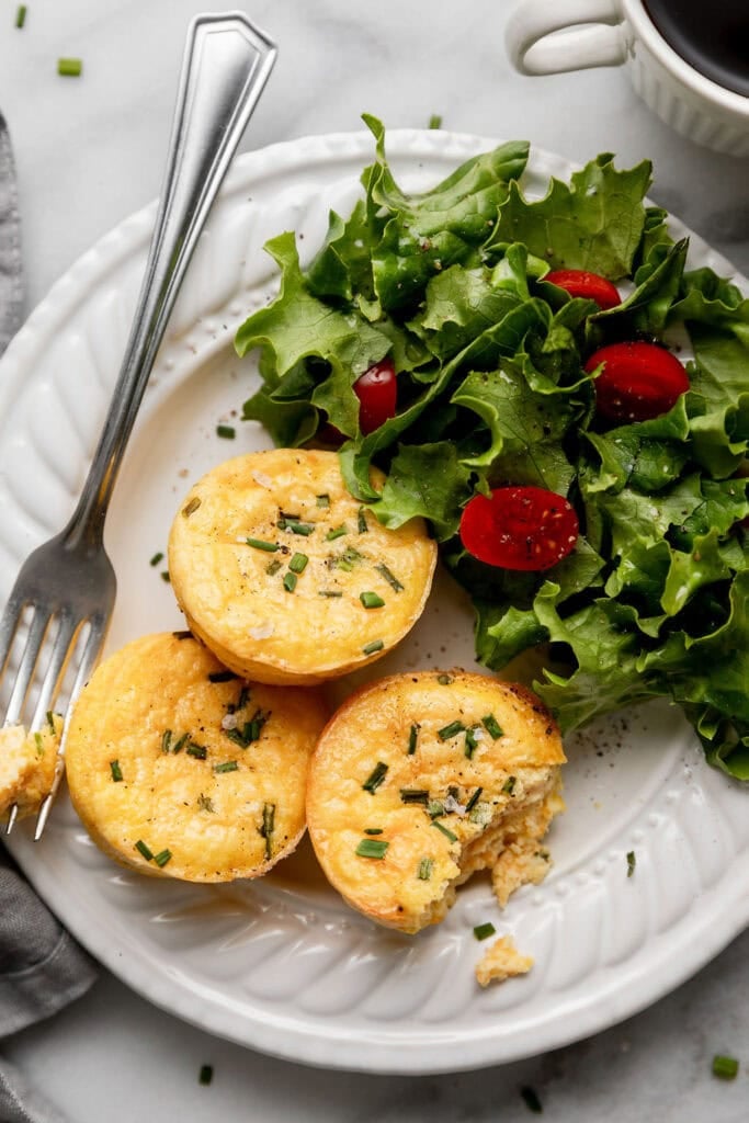 Close up view of a plate of egg bites with fresh salad topped with cherry tomatoes. 