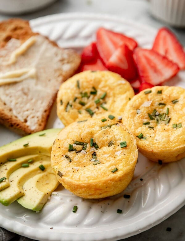 Side view of three cottage cheese egg bites on a plate with strawberries, avocado slices, and toast