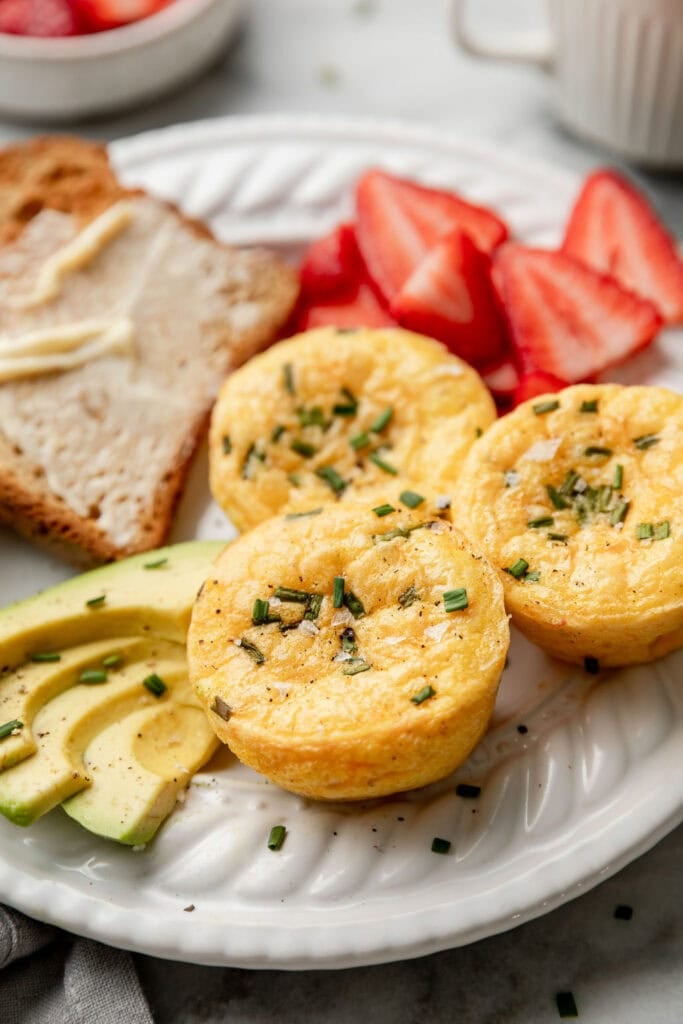 Close up view of egg bites served with fresh strawberries and buttered toast garnished with sliced avocado. 