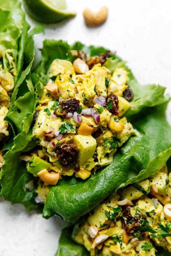A vibrant yellow chicken salad flavored with curry powder and studded with apples and raisins tucked into lettuce wraps ready for serving.