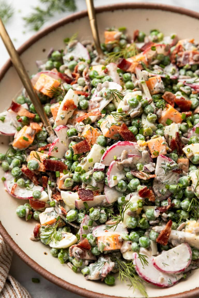 Overhead view of a serving bowl filled with creamy pea salad topped with crispy bacon pieces. 