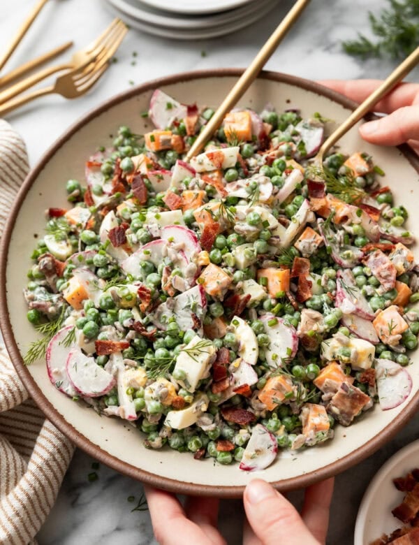 Side view of creamy pea salad with bacon pieces in a large serving bowl