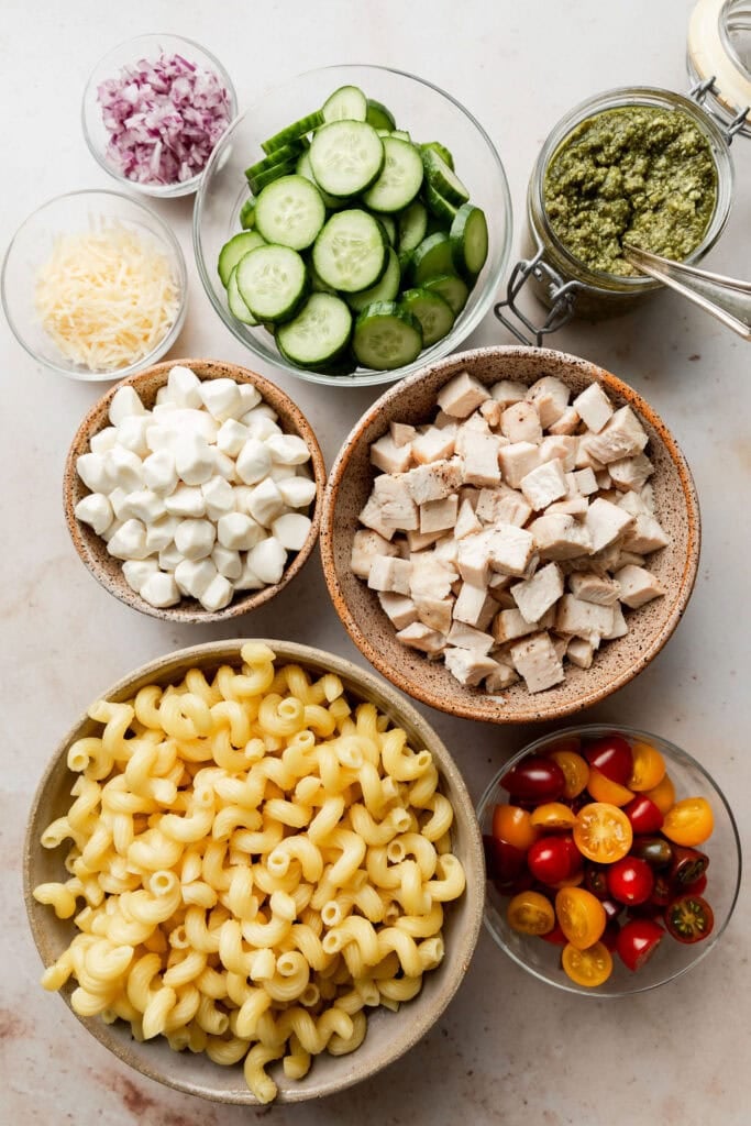 All ingredients for chicken pesto pasta salad in separate bowls arranged together in a cluster