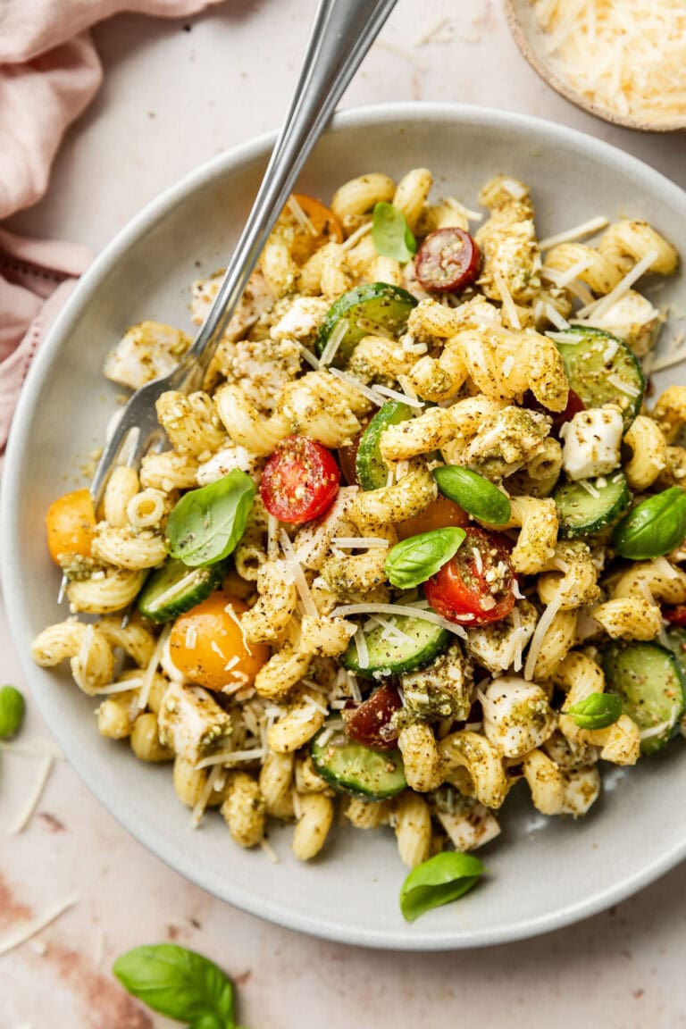 Overhead view of a plate filled with colorful chicken salad tossed in a pesto sauce and topped with fresh basil and shredded parmesan cheese. 