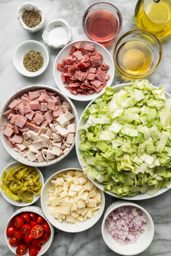 Overhead view of a variety of chopped ingredients for sub in a tub in various bowls including deli meats and lettuce. 