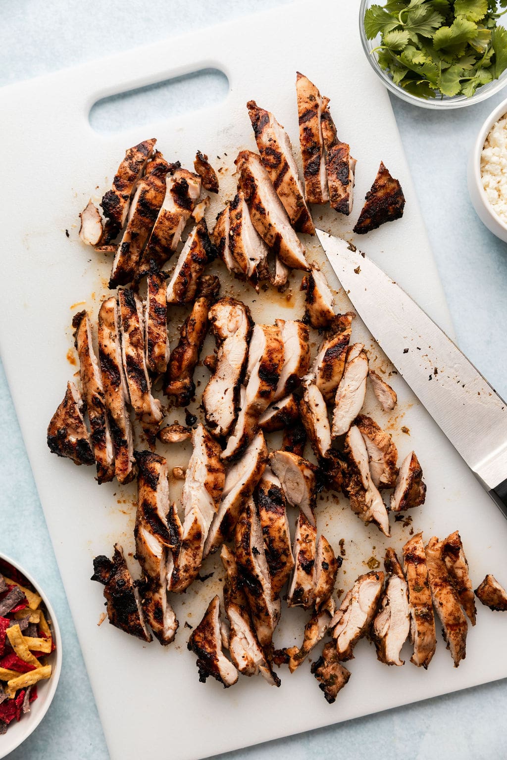 Overhead view of a cutting board filled with sliced grilled chicken with a knife on the side.