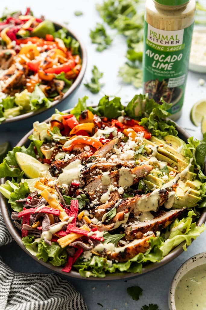 Close up view of a fajita chicken grilled salad topped with avocado lime dressing and crispy tortilla chips. 