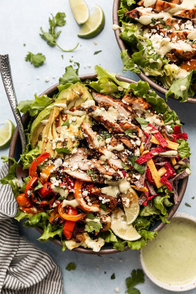 Overhead view of two grilled chicken fajita salads topped with tender grilled vegetables and crispy tortilla chips. 