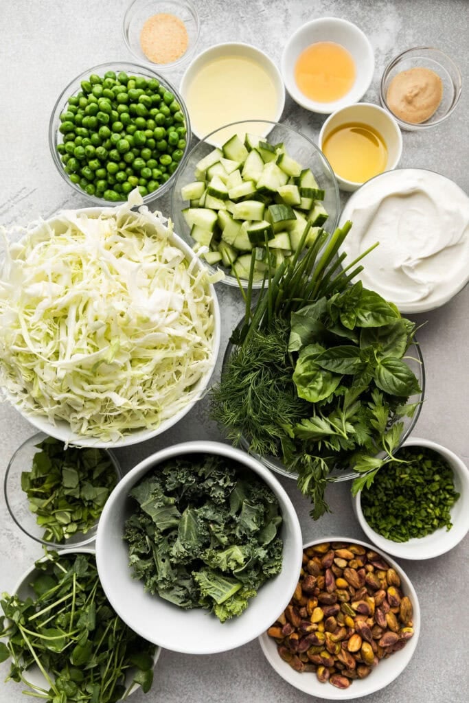 Overhead view of a variety of ingredients for a green goddess salad in different sized bowls. 