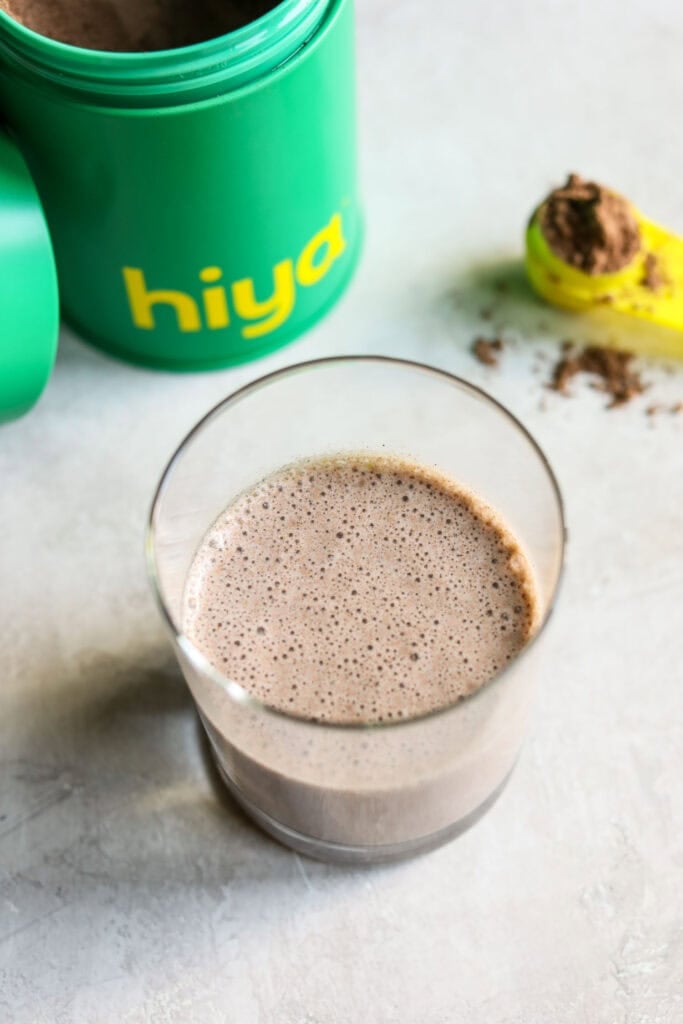 Overhead view of a glass of freshly blended chocolate hiya kids daily greens + superfood powder drink. 