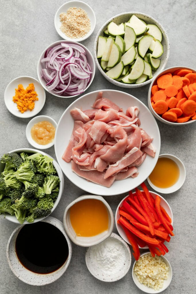 All ingredients for orange pork stir fry arranged in white bowls