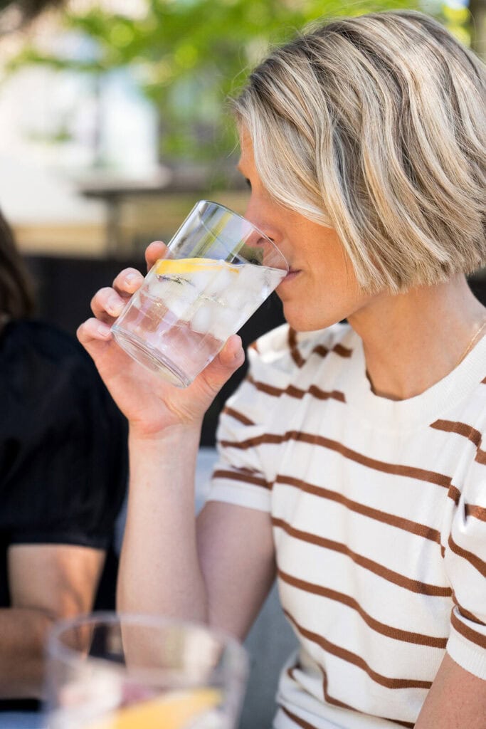 Woman taking a sip of a glass of iced lemon water. 
