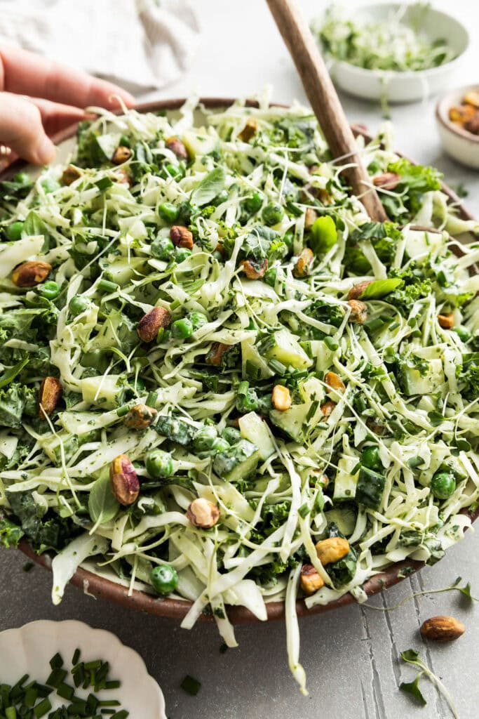 Close up view of a large bowl of green goddess salad topped with fresh green herbs and pistachios.