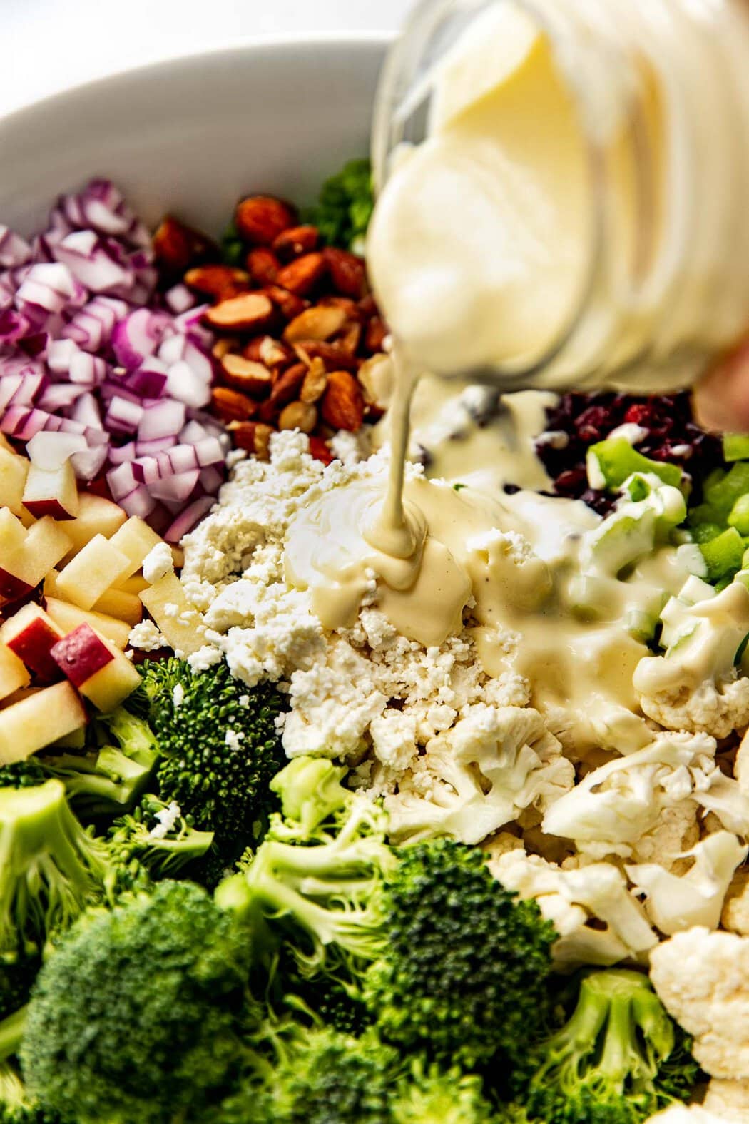 Lemony dressing being poured over ingredients for apple broccoli cauliflower salad in bowl