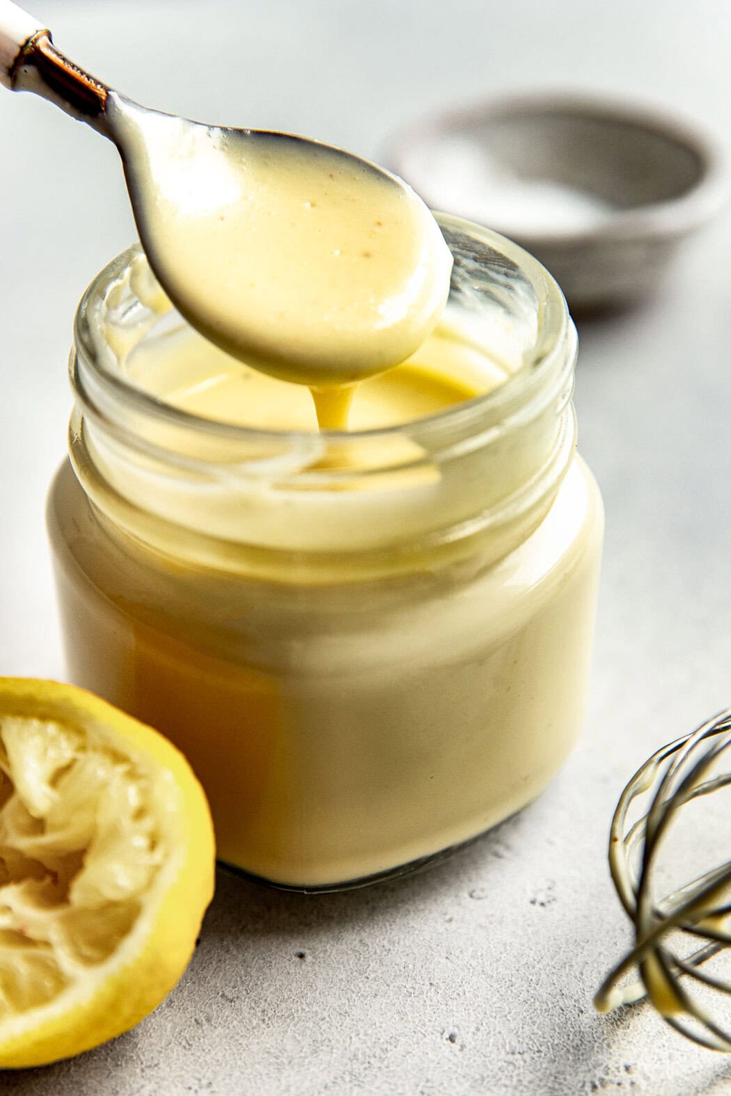 Creamy lemon dressing for apple broccoli salad being scooped up with a spoon from a jar