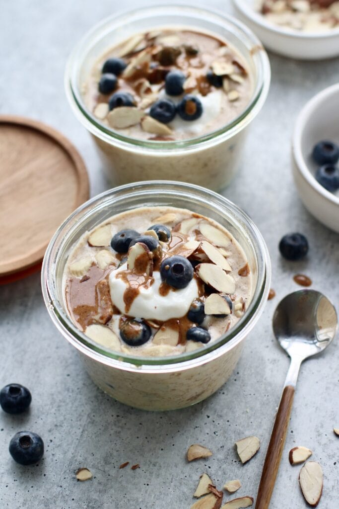 Overhead view of two meal prep containers filled with overnight oats topped with blueberries and nut butter. 