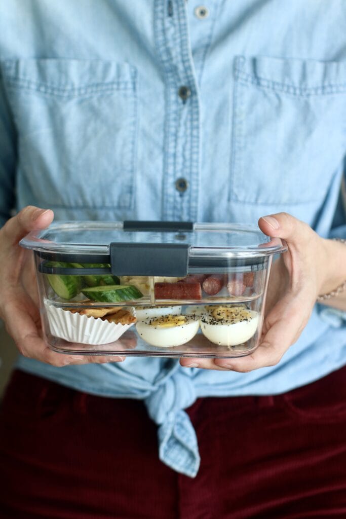 Woman holding a meal prep container filled with separate portions of healthy snacks. 