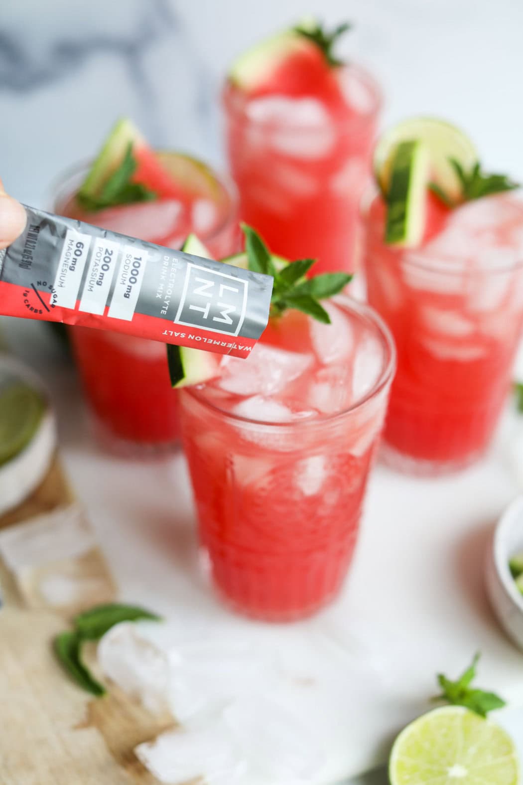 LMNT Watermelon salt packet being poured into a glass of ice and refreshing watermelon electrolyte drink.