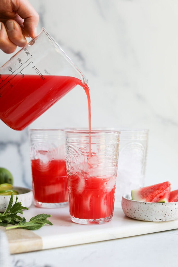 Watermelon juice being poured into tall glasses filled with ice