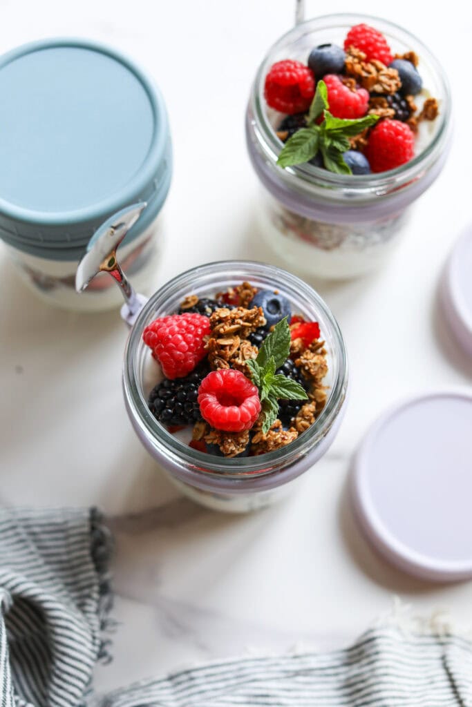 Overhead view of jars with built in spoons for grab and go breakfasts filled with parfaits topped with granola and fruit. 