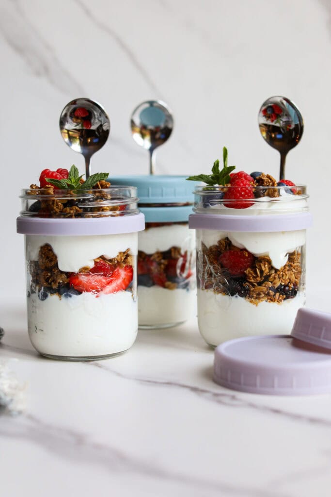 Close up view of jars with built in spoons for grab and go breakfasts filled with layers of fruit parfaits. 