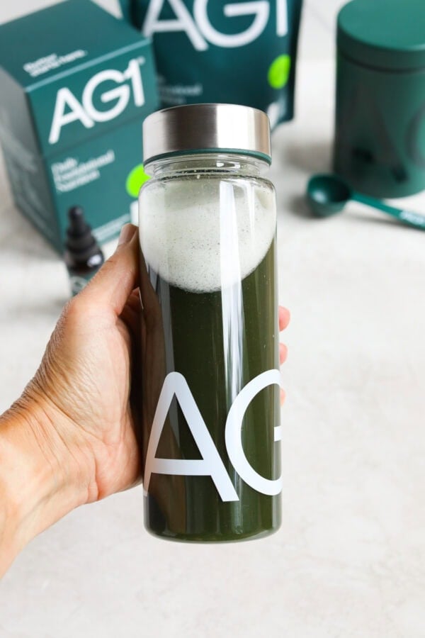 Close up view of a hand holding a bottle of AG1 greens powder mixed in water.
