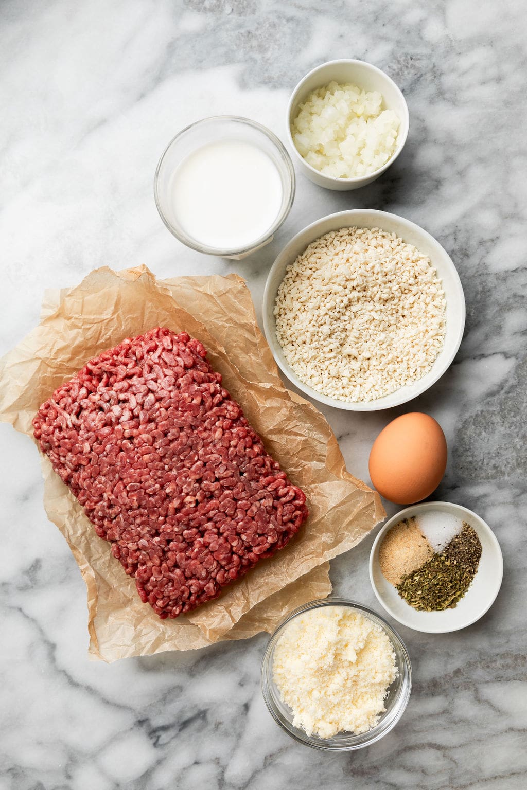 Overhead view of a variety of ingredients for Baked Italian Meatballs, including ground beef and seasonings. 