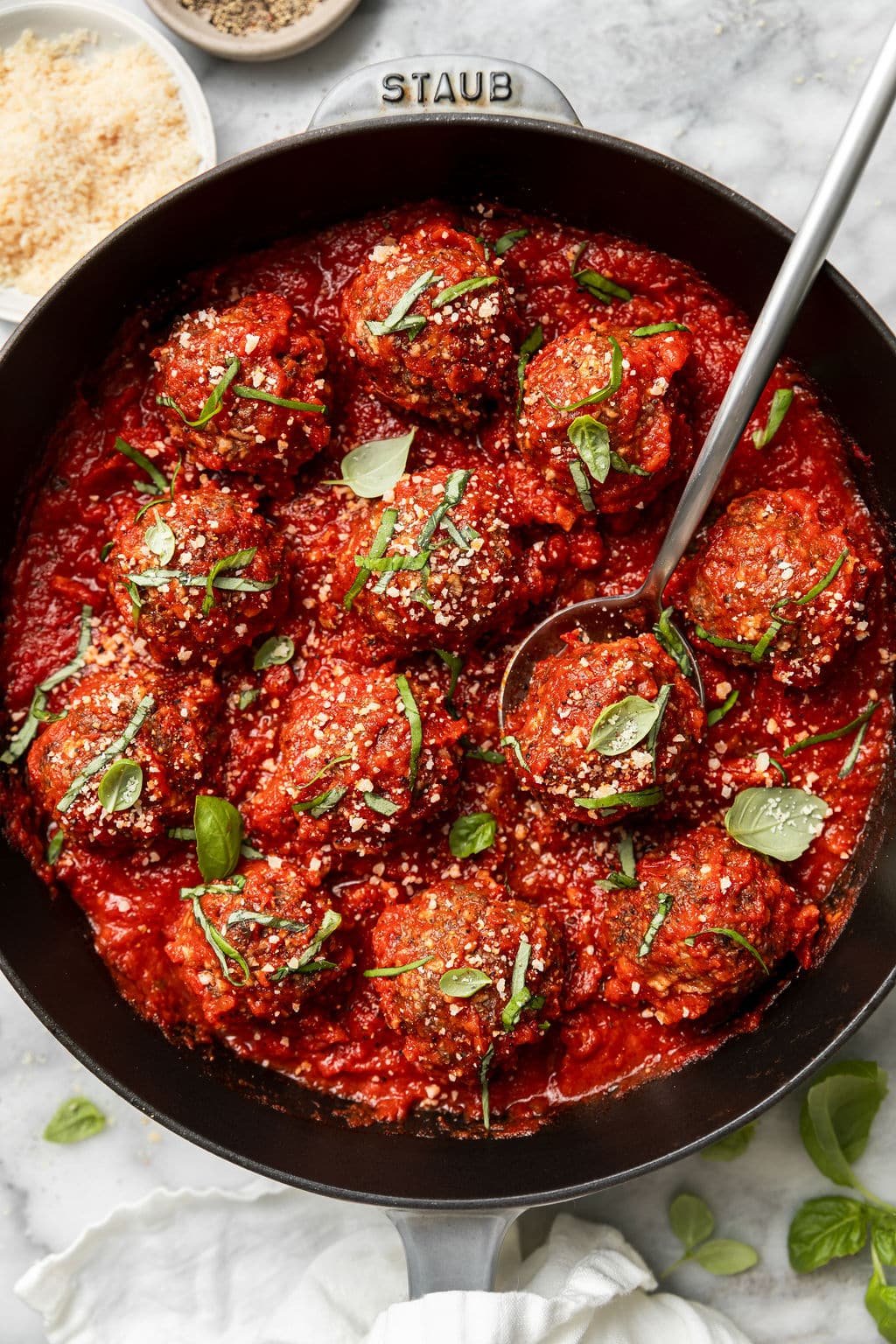 Overhead view of a cast iron skillet filled with Baked Italian Meatballs in a red tomato sauce and topped with fresh basil and parmesan cheese. 