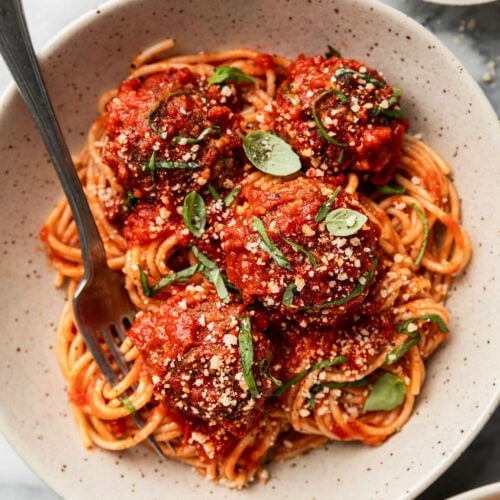 Baked Italian meatballs coated in red sauce over spaghetti noodles in a bowl