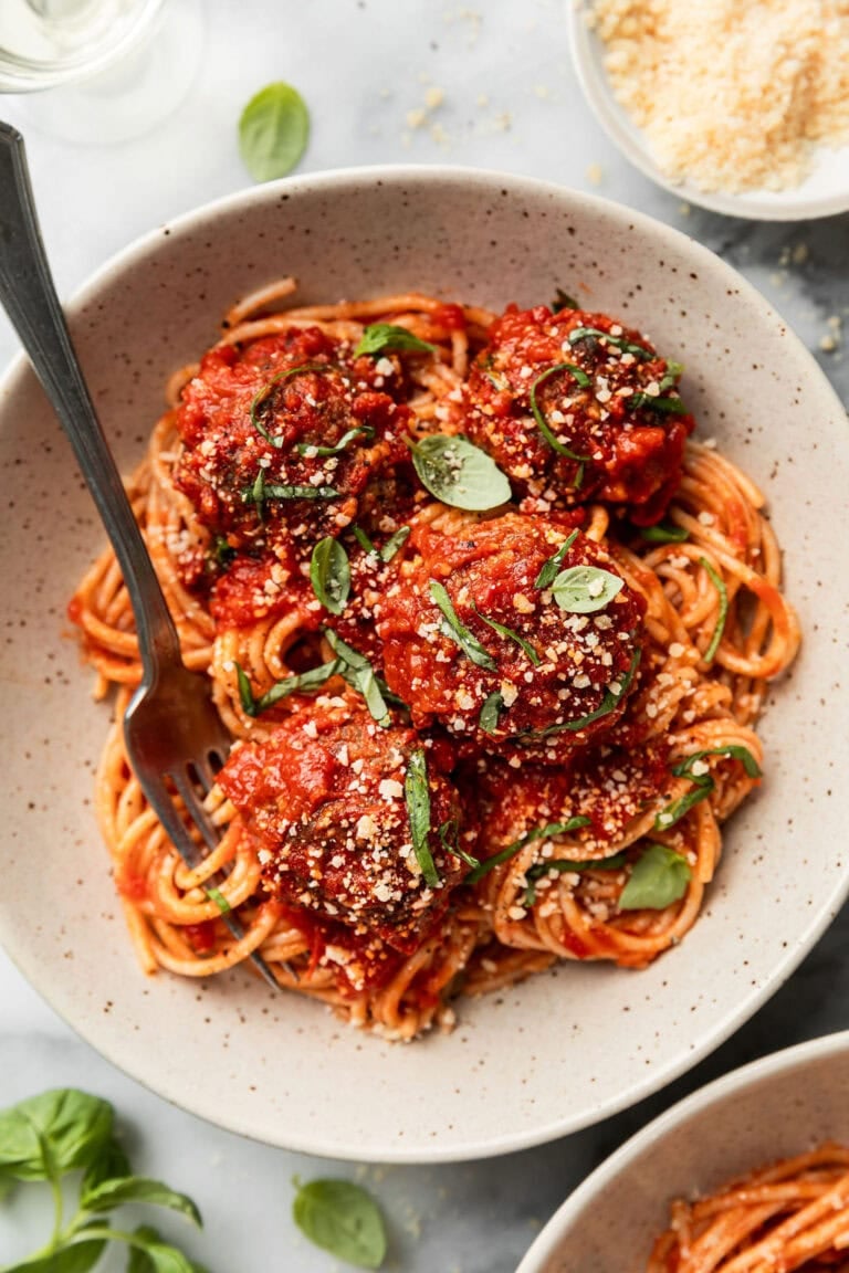 A plate of baked Italian meatballs topped with fresh basil and parmesan cheese. 