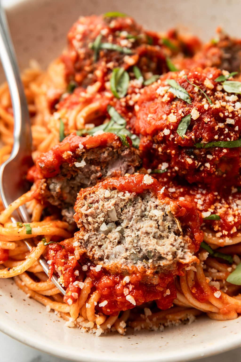 Close up view of a plate of Baked Italian Meatballs and spaghetti noodles topped with fresh basil and parmesan cheese. 