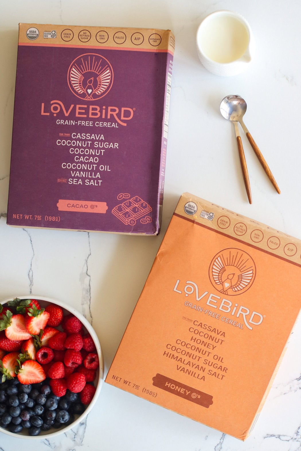 Overhead view of two boxes of love bird cereals next to a bowl of fresh berries. 