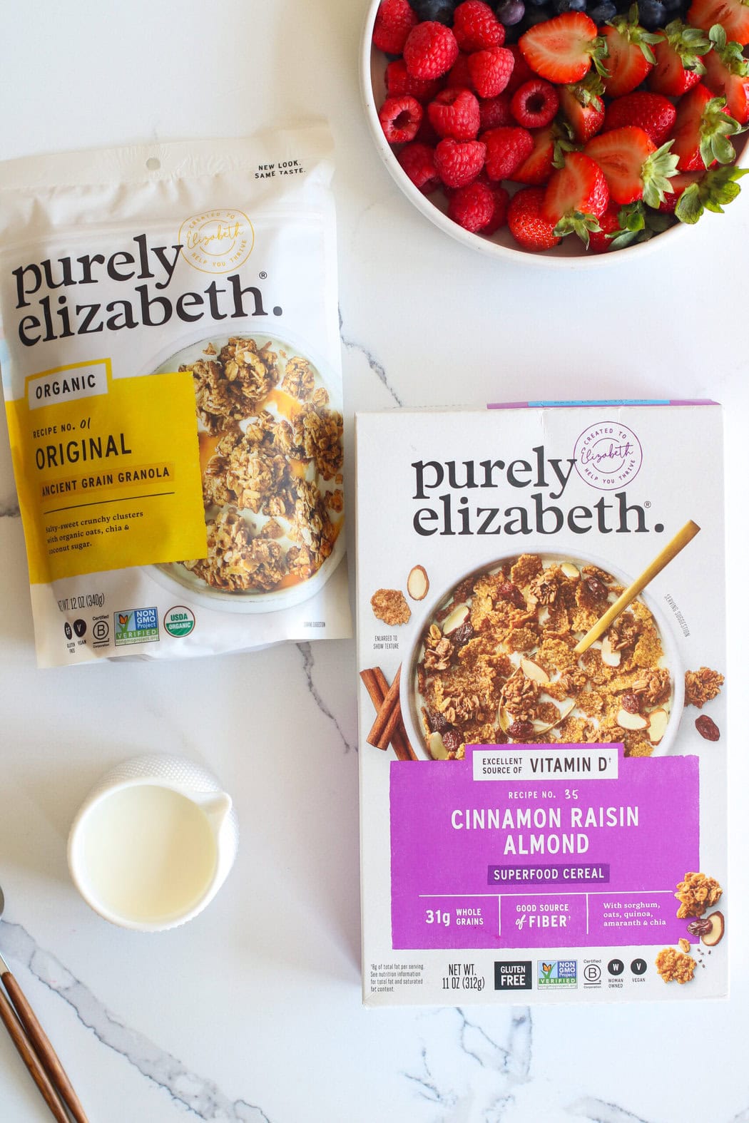 Overhead view of two varieties of purely elizabeth cereals next to fresh berries and milk. 