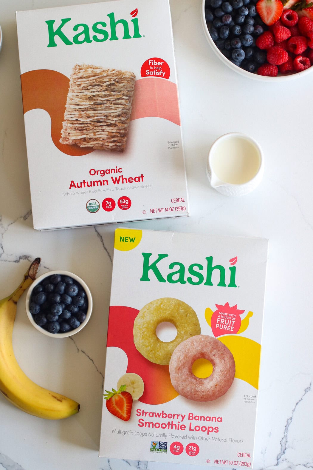 Overhead view of two boxes of Kashi cereals with fresh fruit and milk surrounding them. 