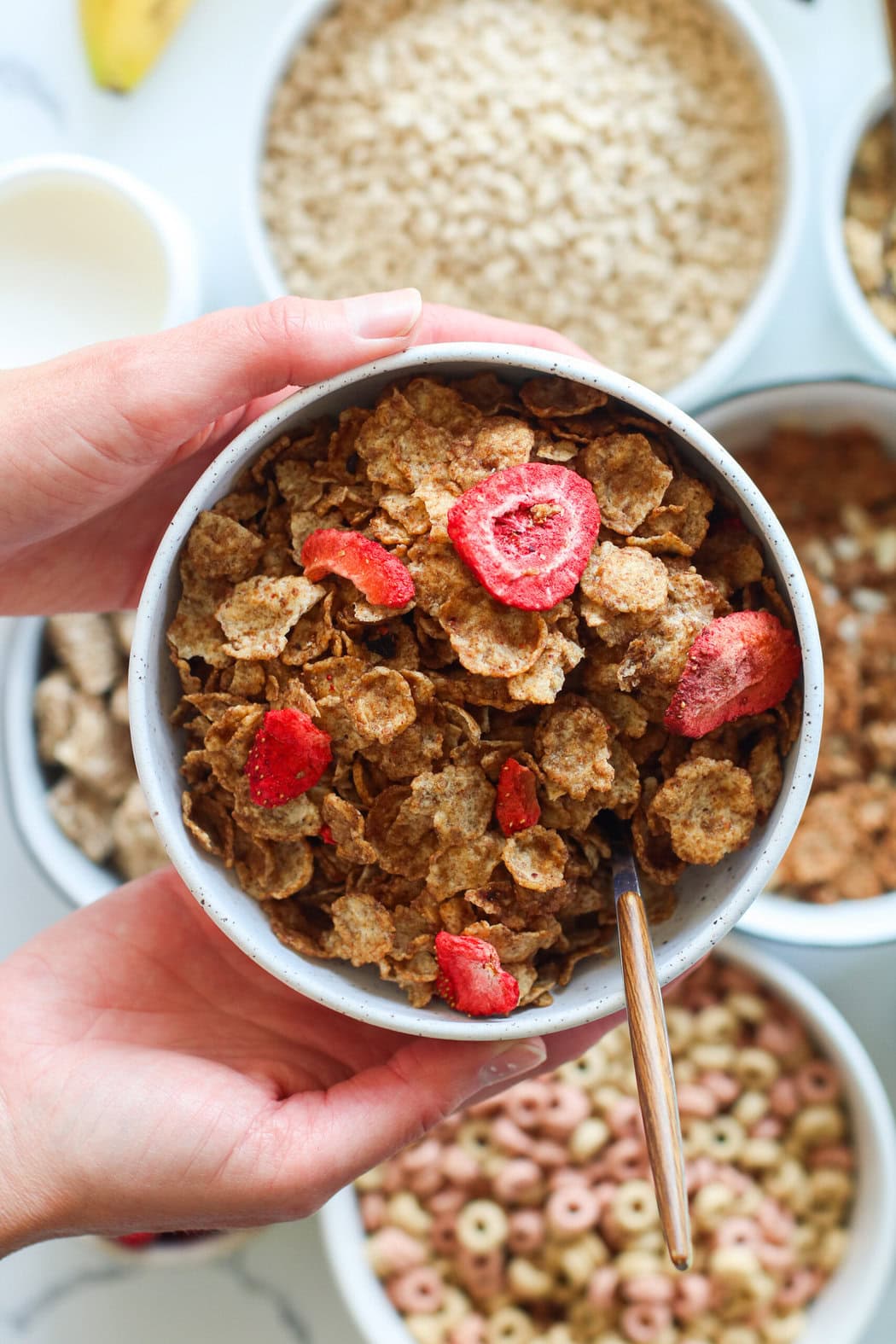 Two hands holding a bowl of cereal topped with strawberries. 