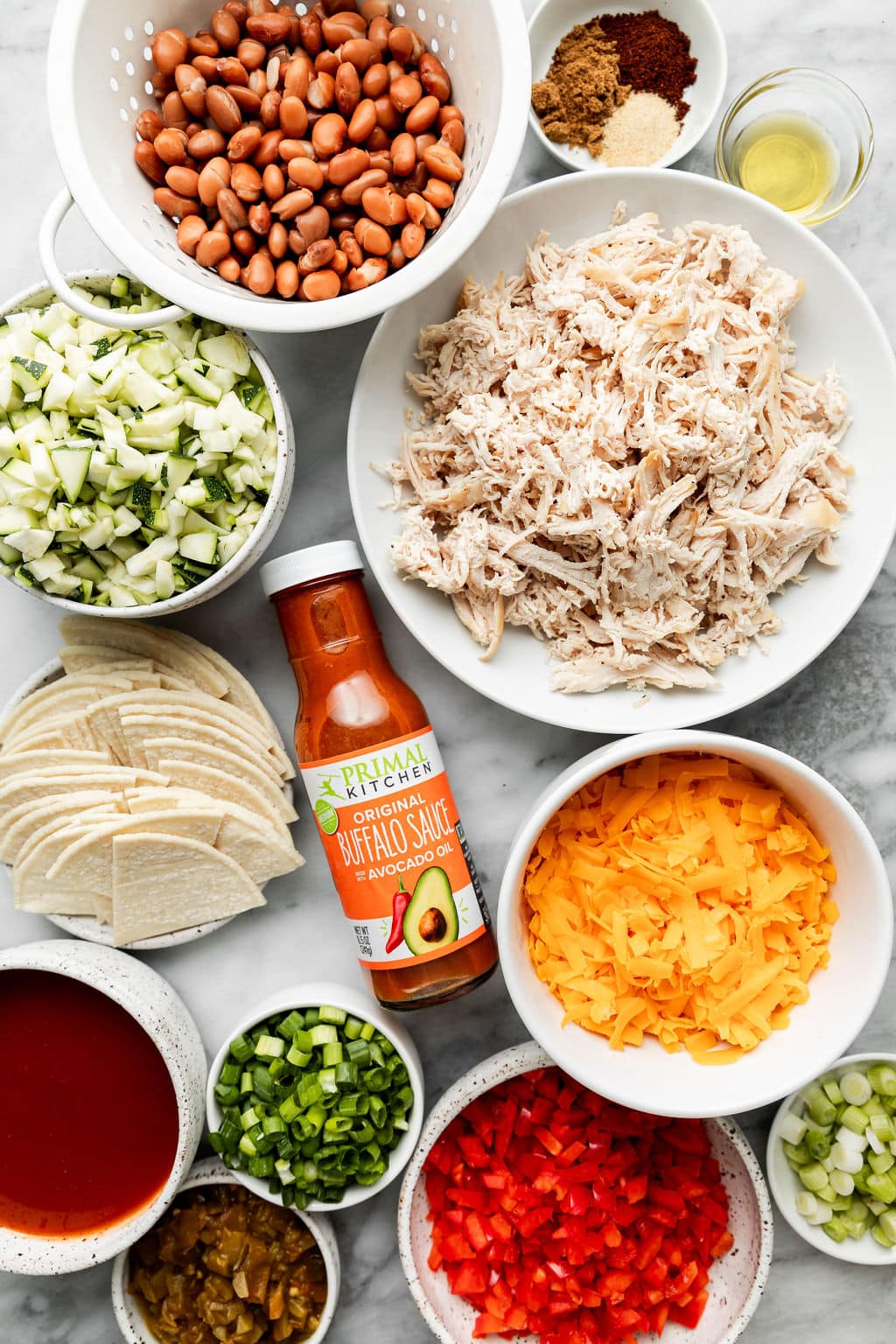 Overhead view of the ingredients for Easy Buffalo Chicken Enchiladas in a variety of bowls. 