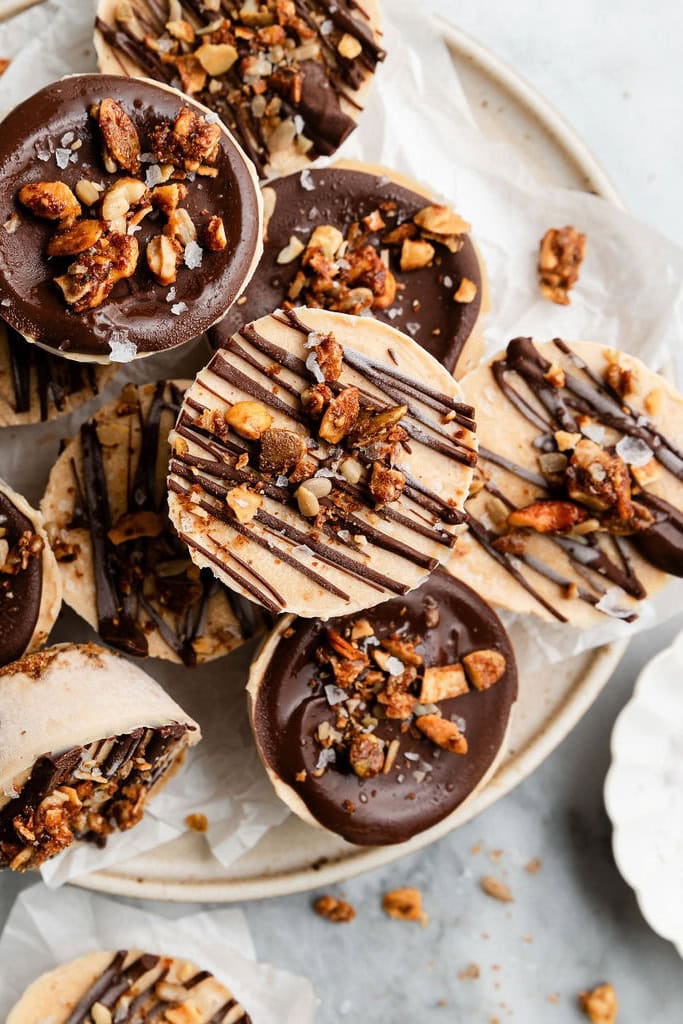 Frozen protein peanut butter cups topped with chocolate and granola stacked up on a plate.