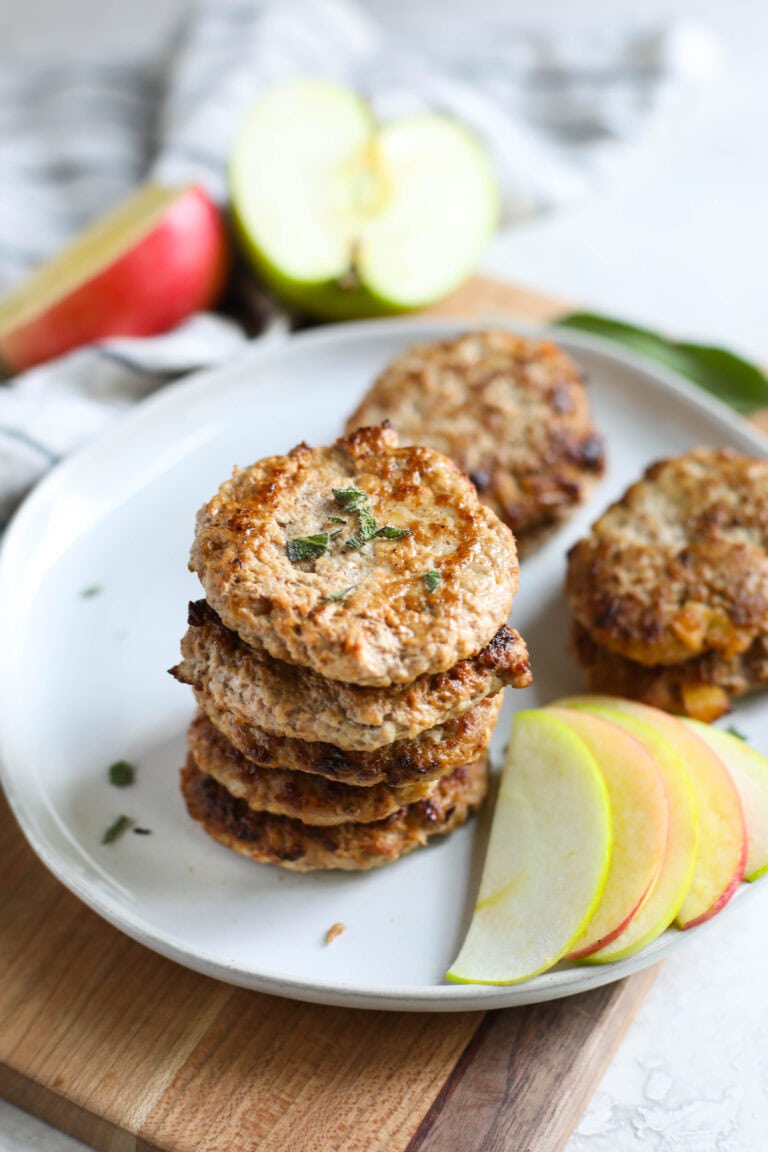 A stack of turkey apple sausage patties with fresh apple slices on the side.