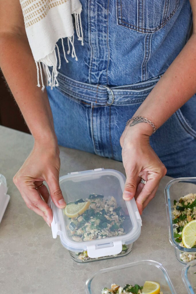 A woman placing a lid on a glass meal prep container filled with a healthy fresh salad. 