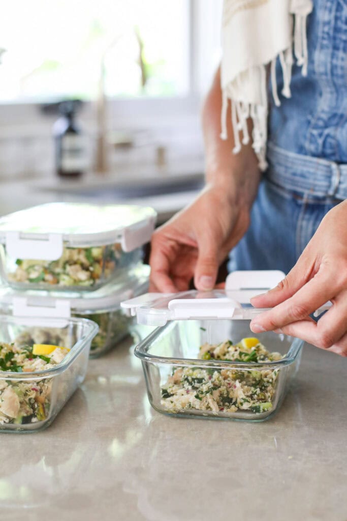 Close up view of a lid being put on a glass meal prep container filled with a fresh salad. 