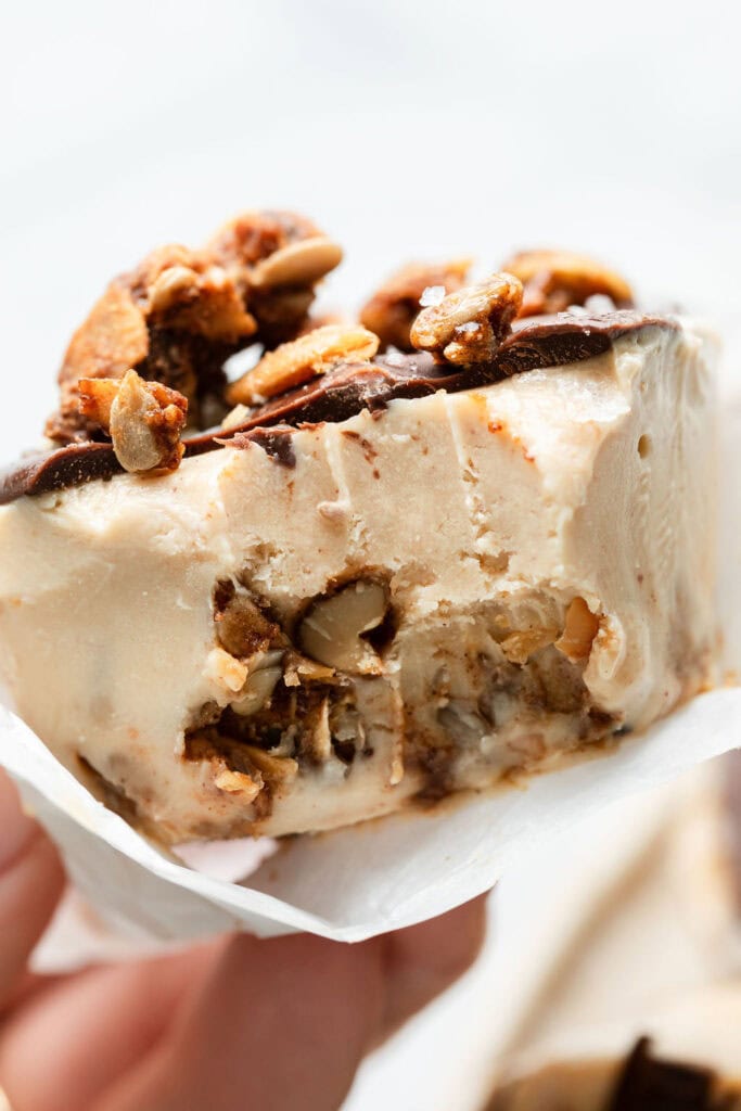 Close up view of a hand holding a Delicious Frozen Yogurt Peanut Butter Cup with a bite out of it to show the layers.