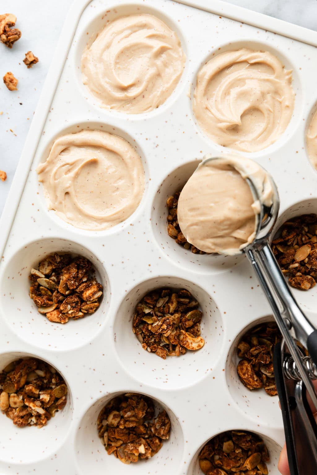 Overhead view of a muffin pan being filled with layers of Delicious Frozen Yogurt Peanut Butter Cups. 