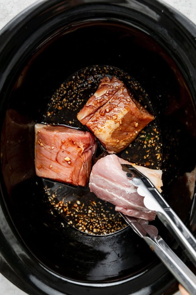 Overhead view of pork and marinade in a slow cooker. 