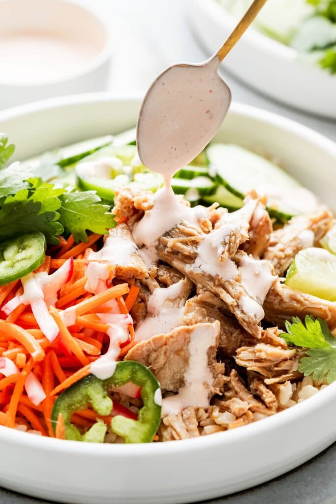 Close up view of a Slow Cooker Banh Mi Rice Bowl being drizzled with spicy dressing.