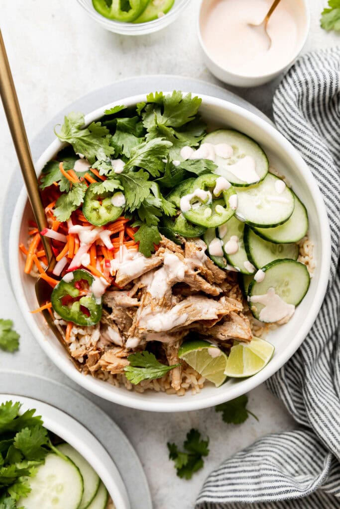 Overhead view of a bowl filled with Slow Cooker Banh Mi ingredients drizzled with a spicy dressing.