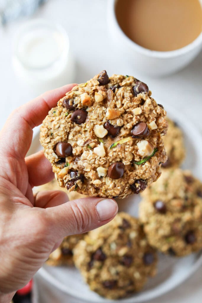 Close up view of a hand holding a Delicious Zucchini Breakfast Cookie filled with walnut pieces and chocolate chips. 