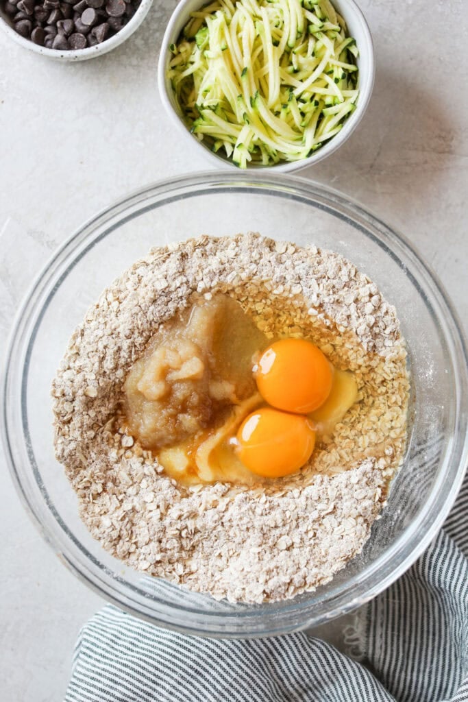 Overhead view of a glass bowl containing ingredients for Zucchini Breakfast Cookies, ready for mixing.