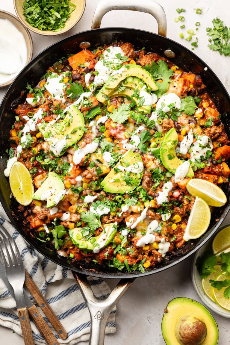 A skillet filled with ground beef and zucchini skillet topped with sour cream and avocado slices. 